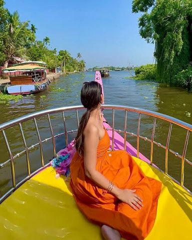 A guest sitting at the bow of a boat on a green village canal lined with palms