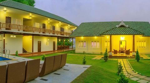 Loungers by the pool facing a lawn and a Kerala-style cottage with a tiled roof
