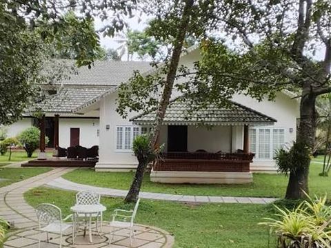 A white cottage with a sloping tiled roof and a garden table under the trees