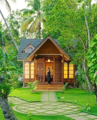 A wooden cottage with arched windows in a green garden of palms