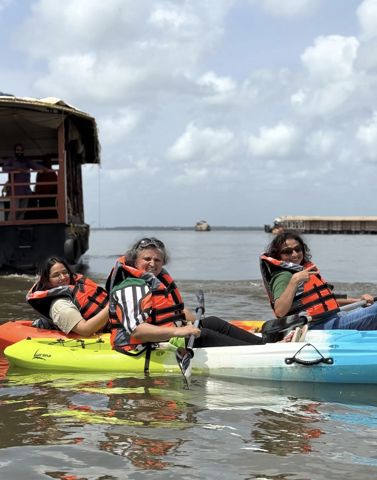 Three guests in life jackets in kayaks on the lake, with a houseboat behind them