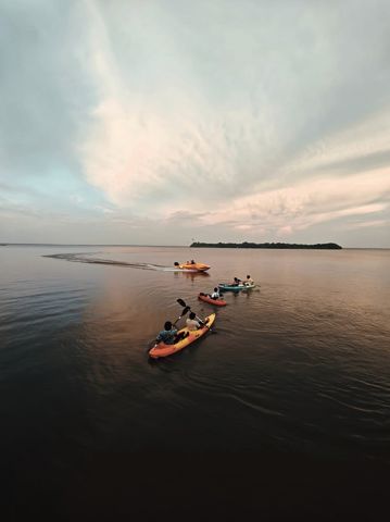 Kayaks and a speedboat heading across calm water toward Pathiramanal island at dusk