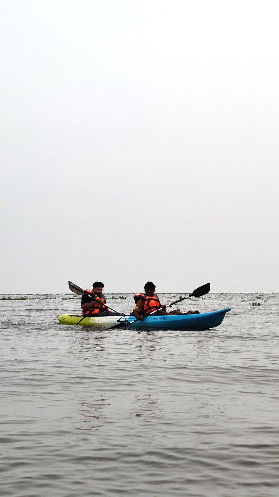 Two kayakers in life jackets on a hazy lake