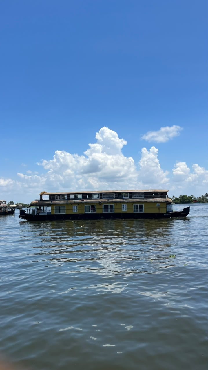 Our premium two-deck houseboat, yellow with a long upper deck, on the lake under a blue sky with white clouds
