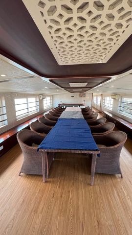 A long dining table with wicker chairs and windows on both sides