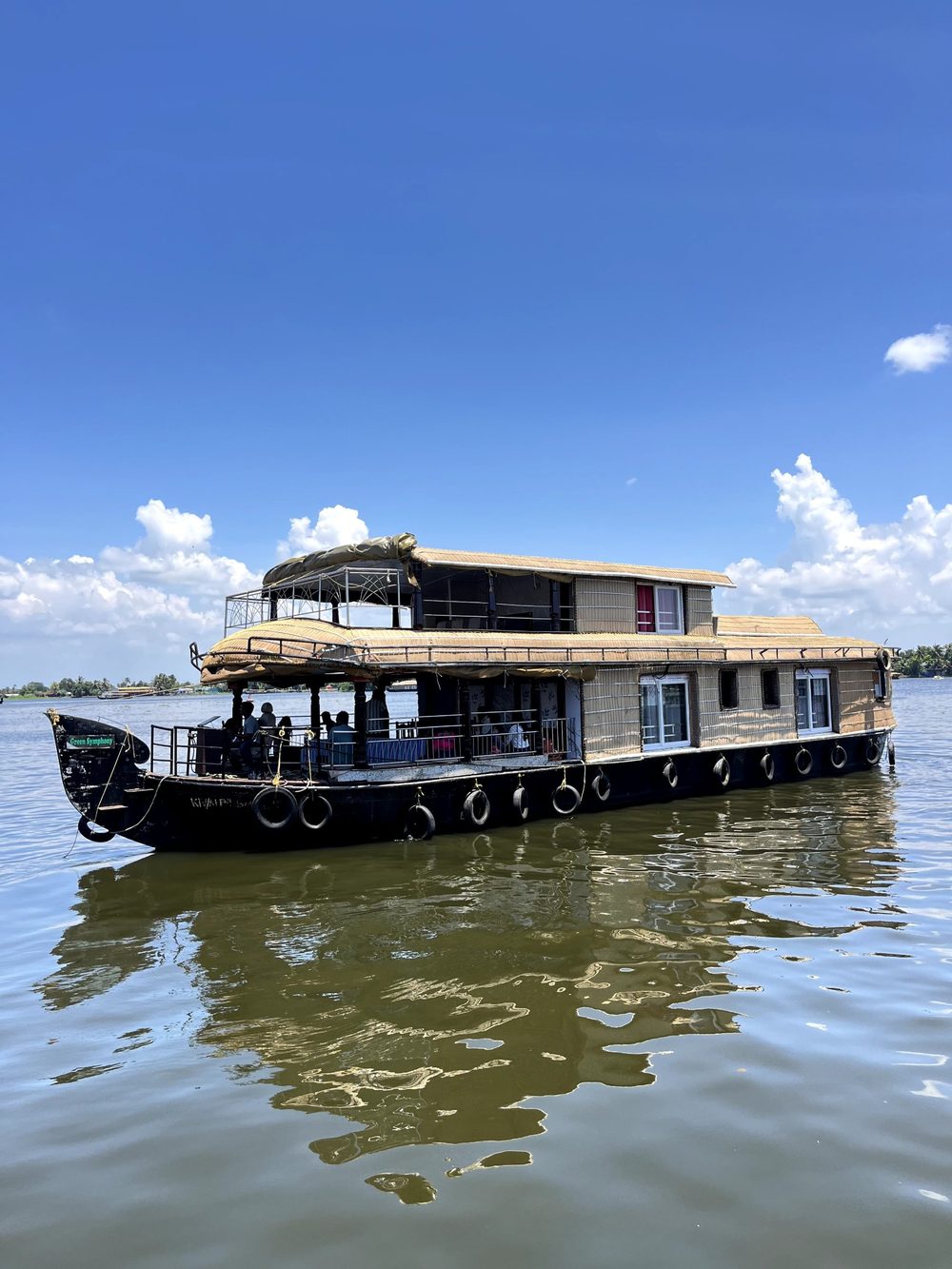 A two-deck houseboat with a woven roof on the lake under a blue sky