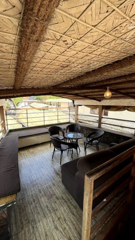 A shaded upper-deck lounge with a woven roof, sofas and chairs