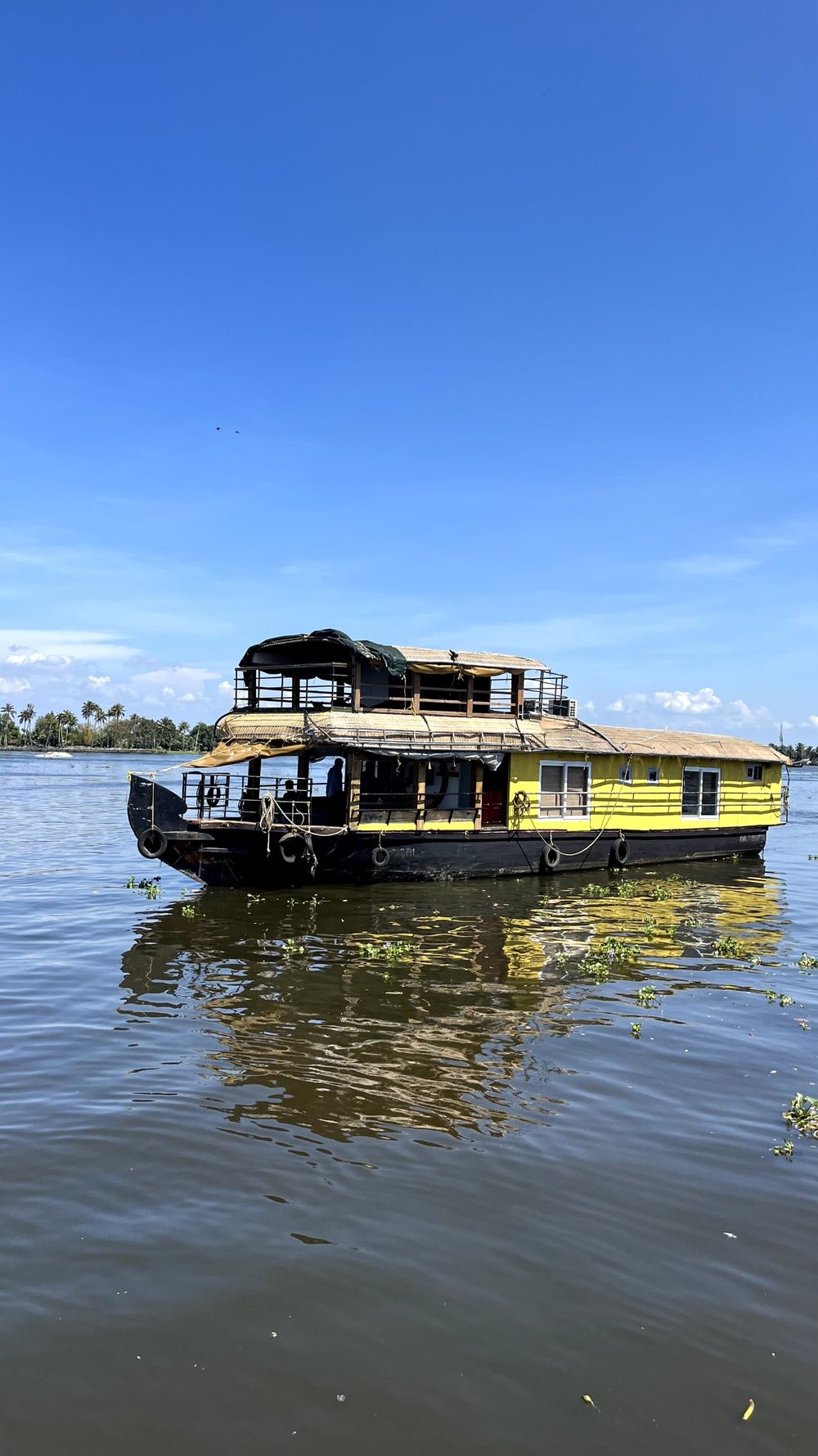 A yellow two-deck houseboat on the lake under a blue sky