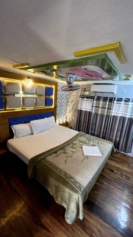 A bedroom with a double bed, a lit padded headboard, curtains and an air-conditioner