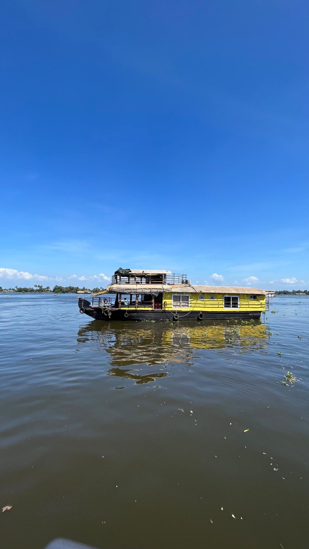 Our standard houseboat, yellow with a two-level thatched roof, on the open lake under a blue sky