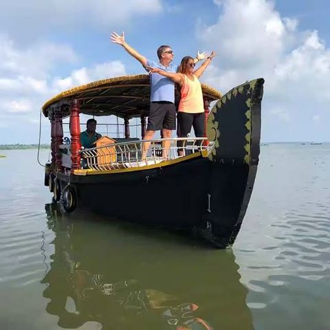 Two guests with arms raised at the bow of a shikara on the lake