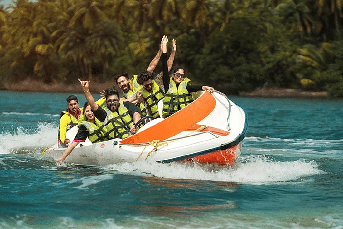 A group in yellow life jackets cheering on a fast white and orange ride boat, spray flying