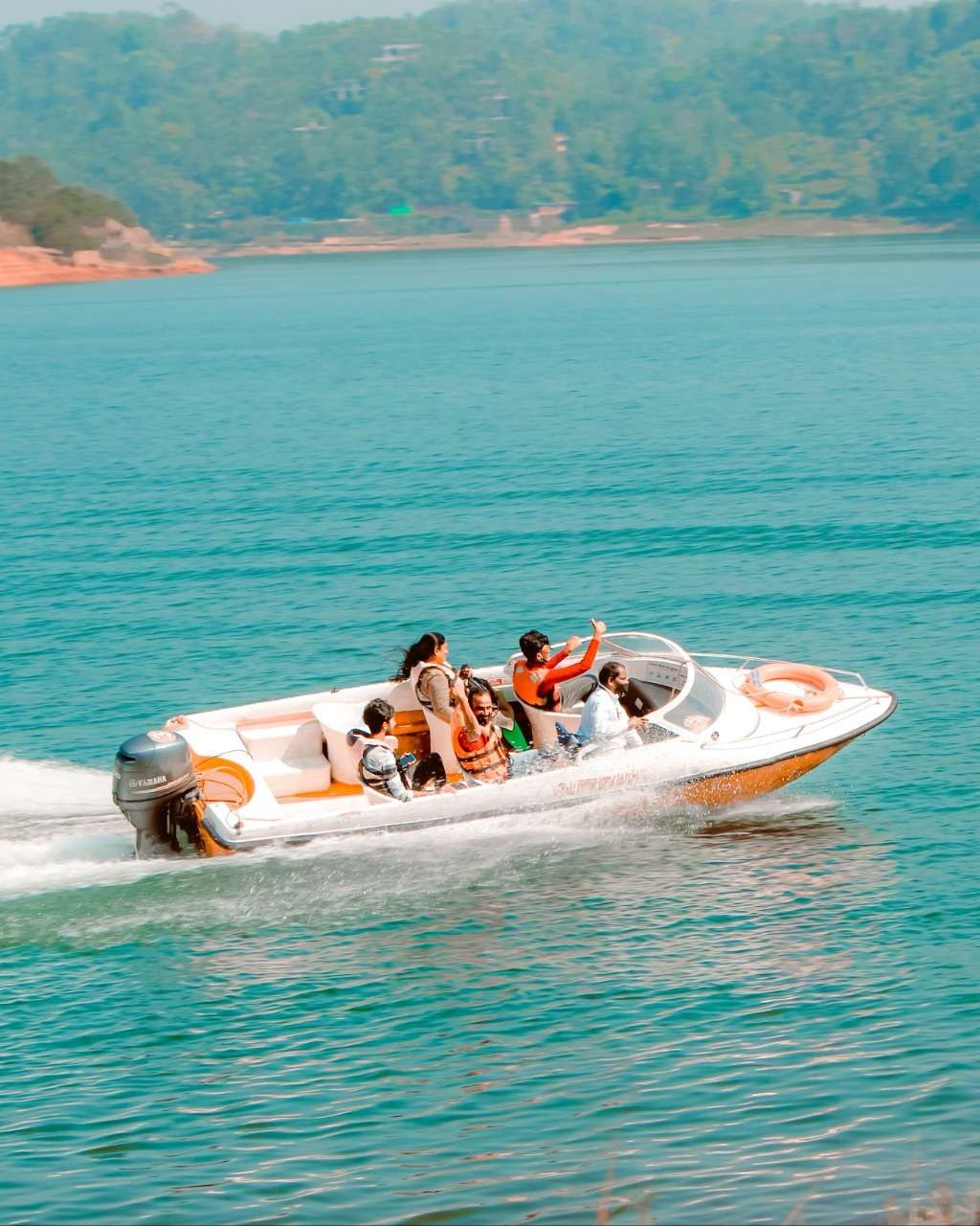 A white speedboat with an outboard motor carrying passengers across blue-green water
