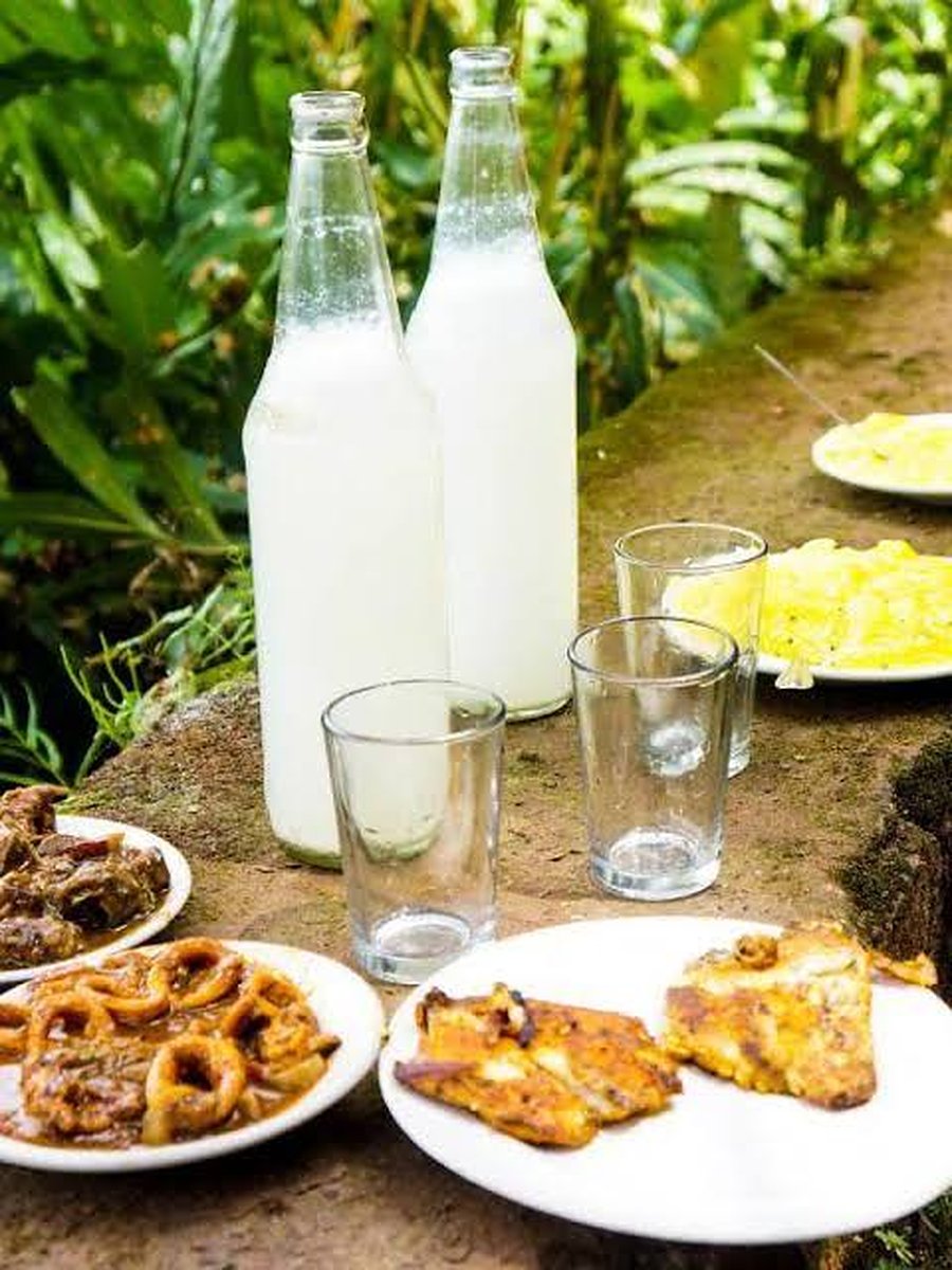 Two bottles of fresh toddy with glasses, squid fry, fish fry, beef and tapioca on a stone ledge